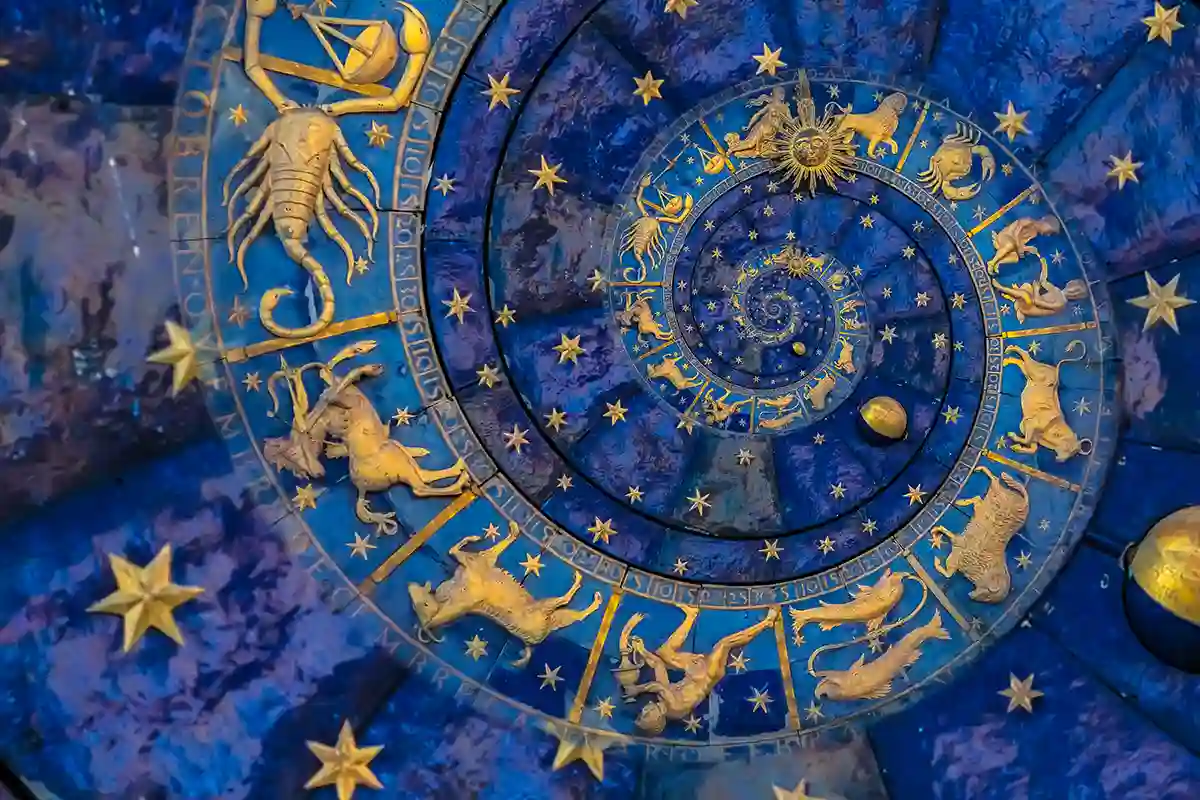 Melsvos ir oranžinės spalvų astrologinis Zodiako ženklų ratas su švytinčiais simboliais bei žvaigždžių linijomis kosminiame fone.