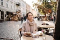 Stilinga moteris sėdi jaukioje kavinėje ir romantiškai šypsodamasi žiūri į priekį, o ore aplink ją sklando šviečiantys auksiniai Zodiako ženklai.