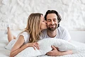 Miegamajame besišypsanti pora – moteris bučiuoja vyrą į žandą. Iliustracija straipsniui apie intymų suderinamumą pagal Zodiako ženklus