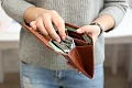 Moters rankos laiko atidarytą rudą odinę piniginę, pripildytą popierinių pinigų kupiūrų. Vaizdas simbolizuoja finansinę gausą, stabilumą ir sėkmę pritraukiant turtus.