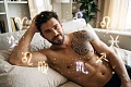 Vyras atsipalaidavęs guli ant sofos, o aplink jį ore sklando švytintys Zodiako ženklų simboliai. Iliustracija straipsniui apie viengungių vyrų ypatumus pagal horoskopą.